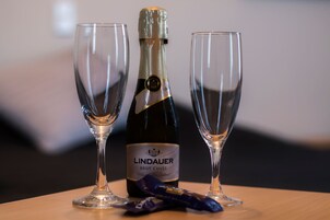 Uma garrafa de espumante Lindauer Brut Cuvée e dois copos vazios sobre uma mesa de madeira.