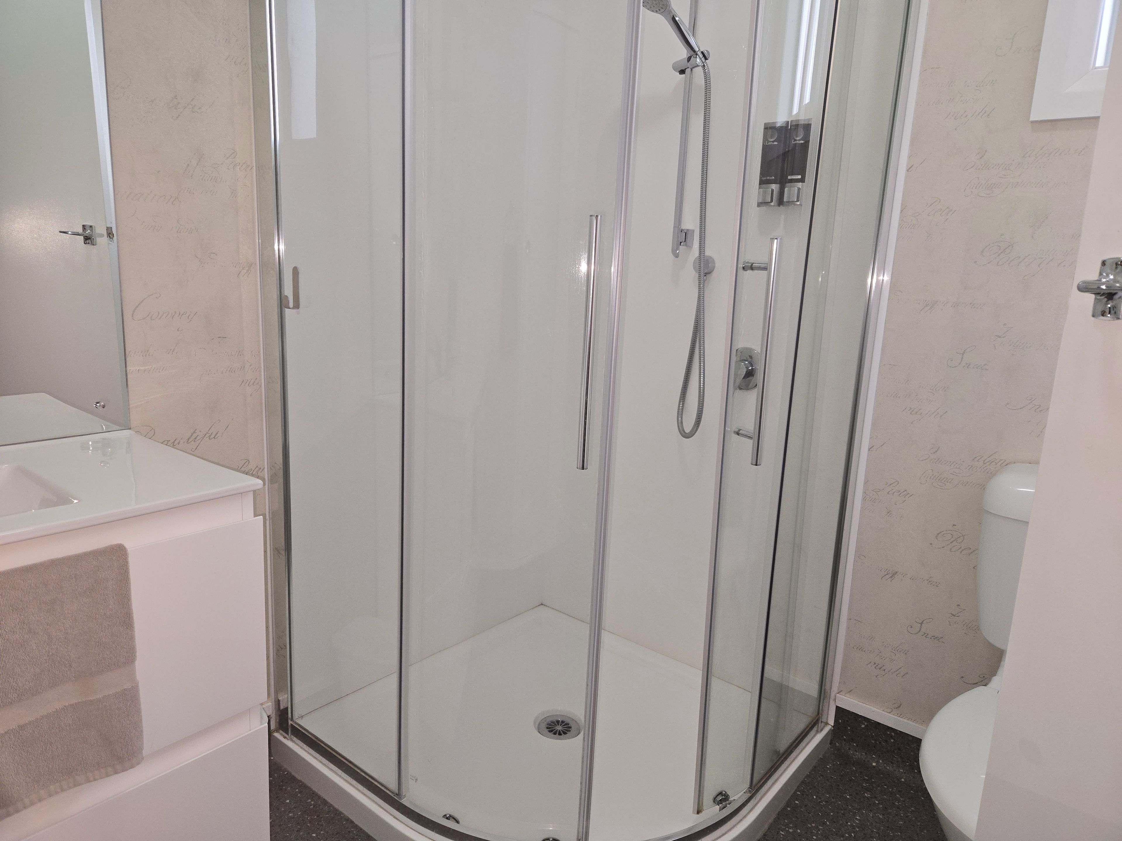 A glass-enclosed shower stall with a handheld showerhead and a wall-mounted control panel.