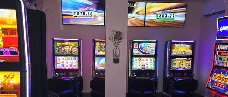 A row of slot machines with digital displays, a pillar with a floral decoration, and a wall-mounted television.