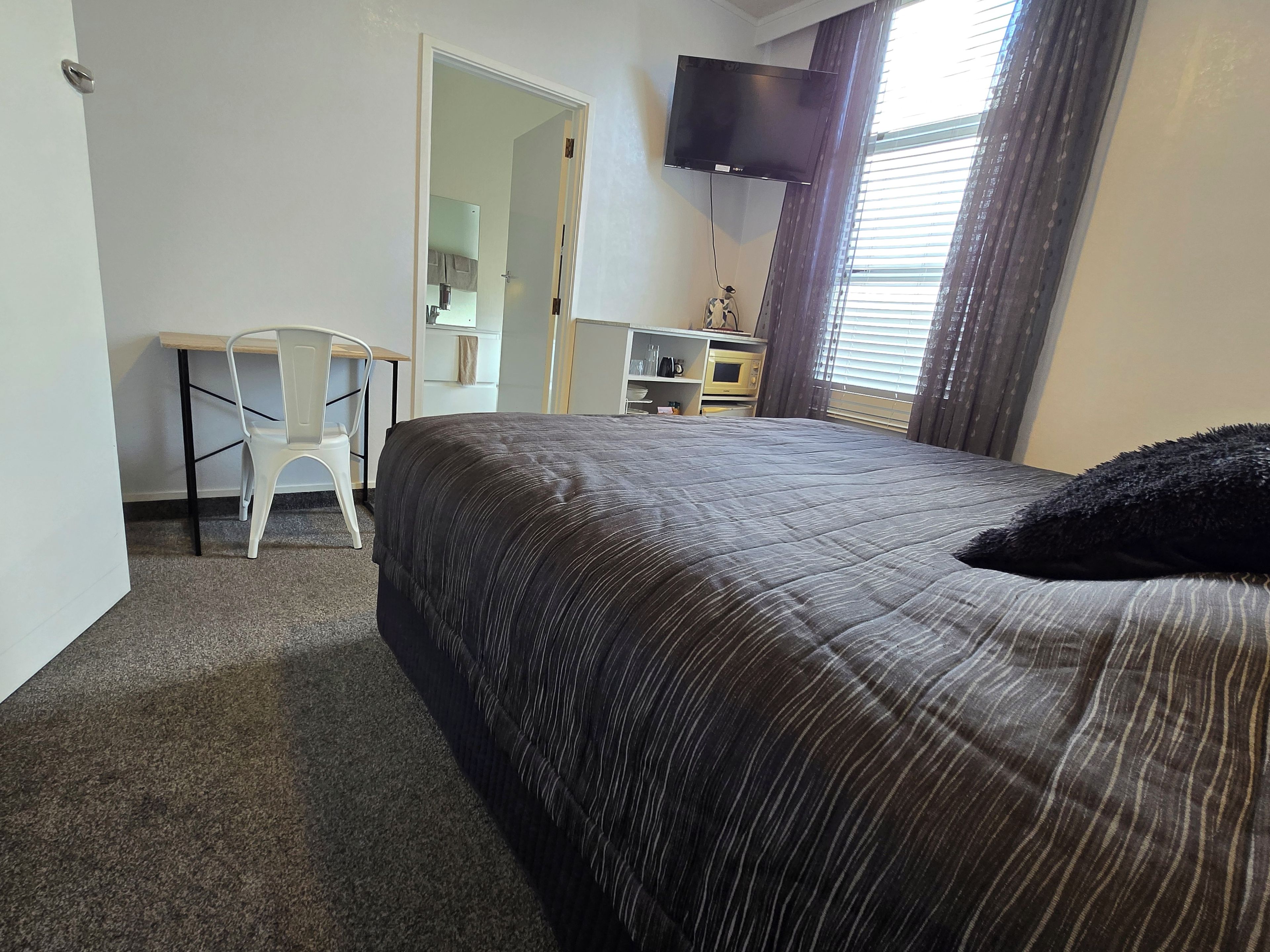 A hotel room with a bed, a desk, a chair, a television, and a window with curtains.
