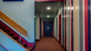 A hallway with a wooden staircase on the left, a red carpet, and a blue door at the end.