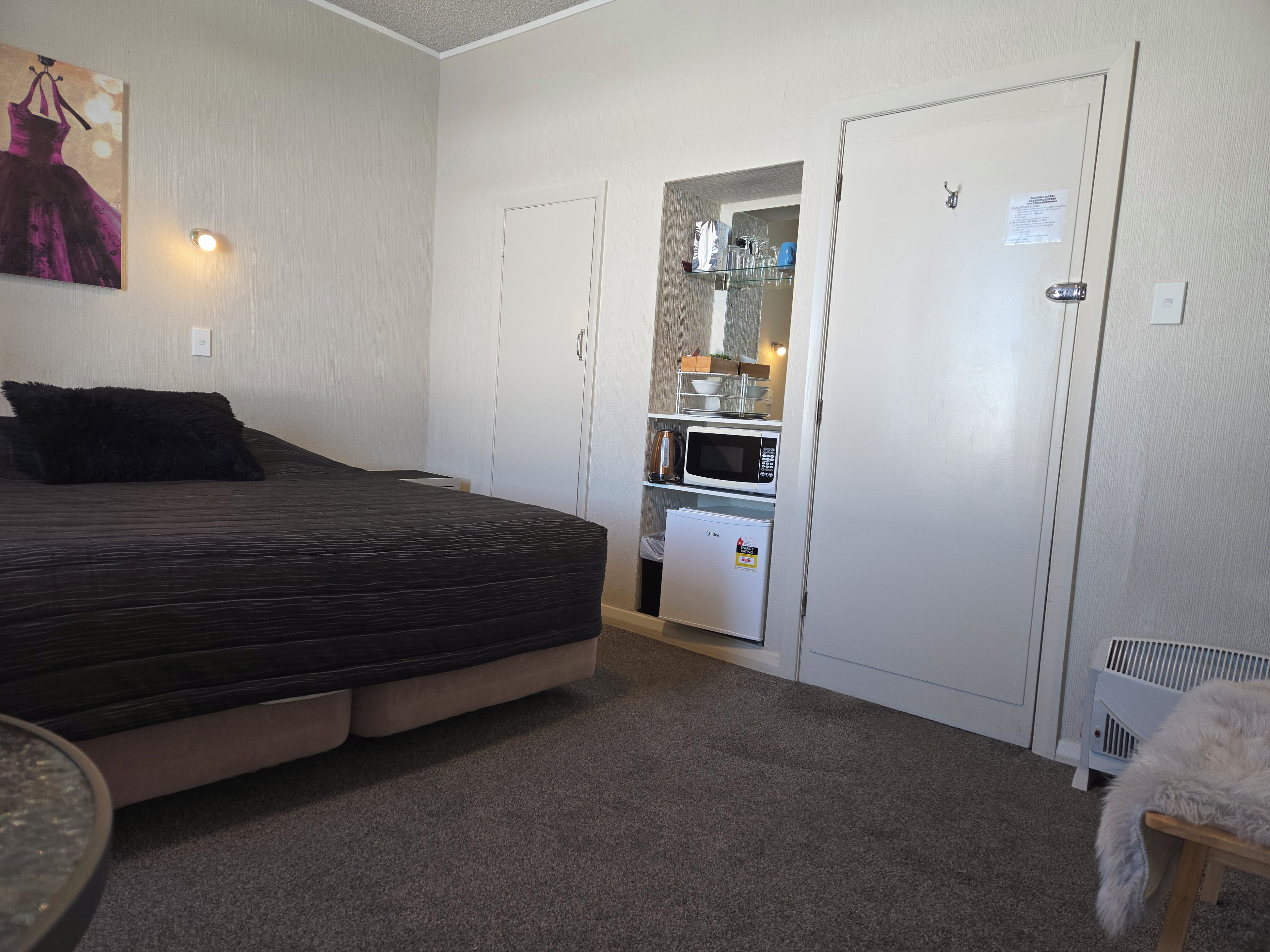 Una habitación pequeña con cama, kitchenette y una puerta que da a otra habitación.
