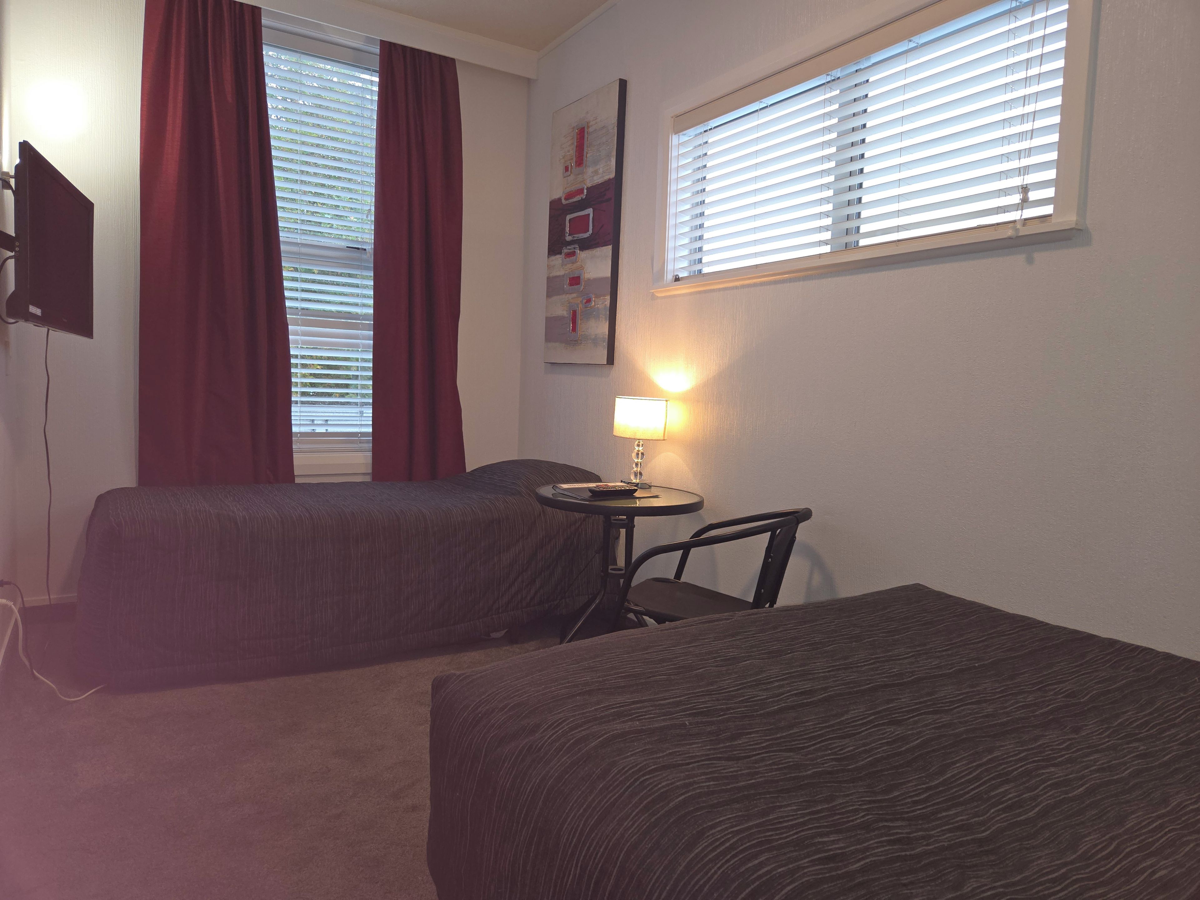 Een hotelkamer met twee bedden, een kleine tafel met een lamp en een aan de muur bevestigde televisie.