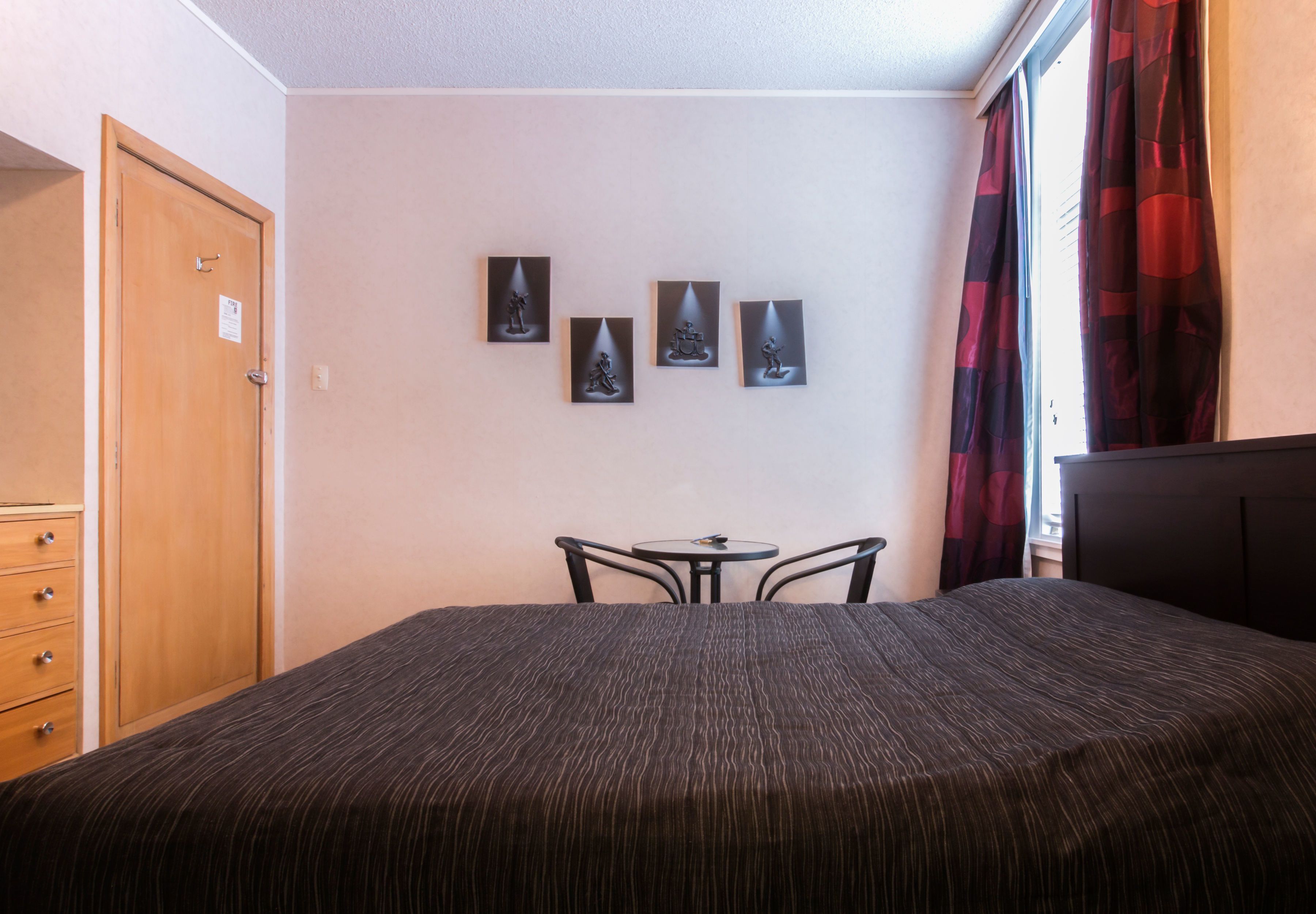 A bedroom with a bed, a small table with two chairs, a wardrobe, and four wall-mounted pictures.