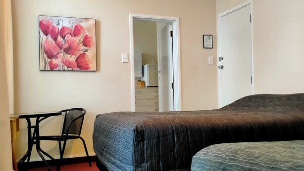 A bedroom with two beds, a desk, a chair, and a painting on the wall.