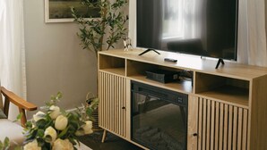 Ett modernt vardagsrum med en platt-TV på ett träställ, en gästbok på ett bord och en vas med blommor.
