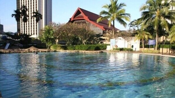 A swimming pool with clear water, surrounded by palm trees and a building with a red roof.