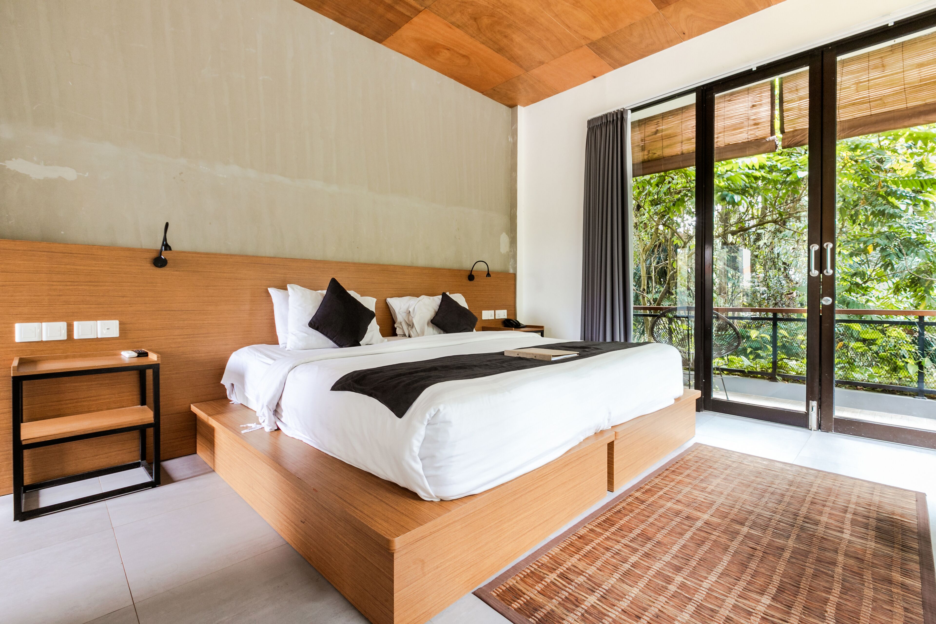 Une chambre moderne avec un lit en bois, une table de chevet et une grande fenêtre donnant sur un paysage verdoyant.