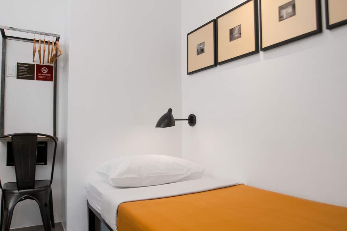 A hotel room with a bed, a chair, a desk, a lamp, and framed pictures on the wall.