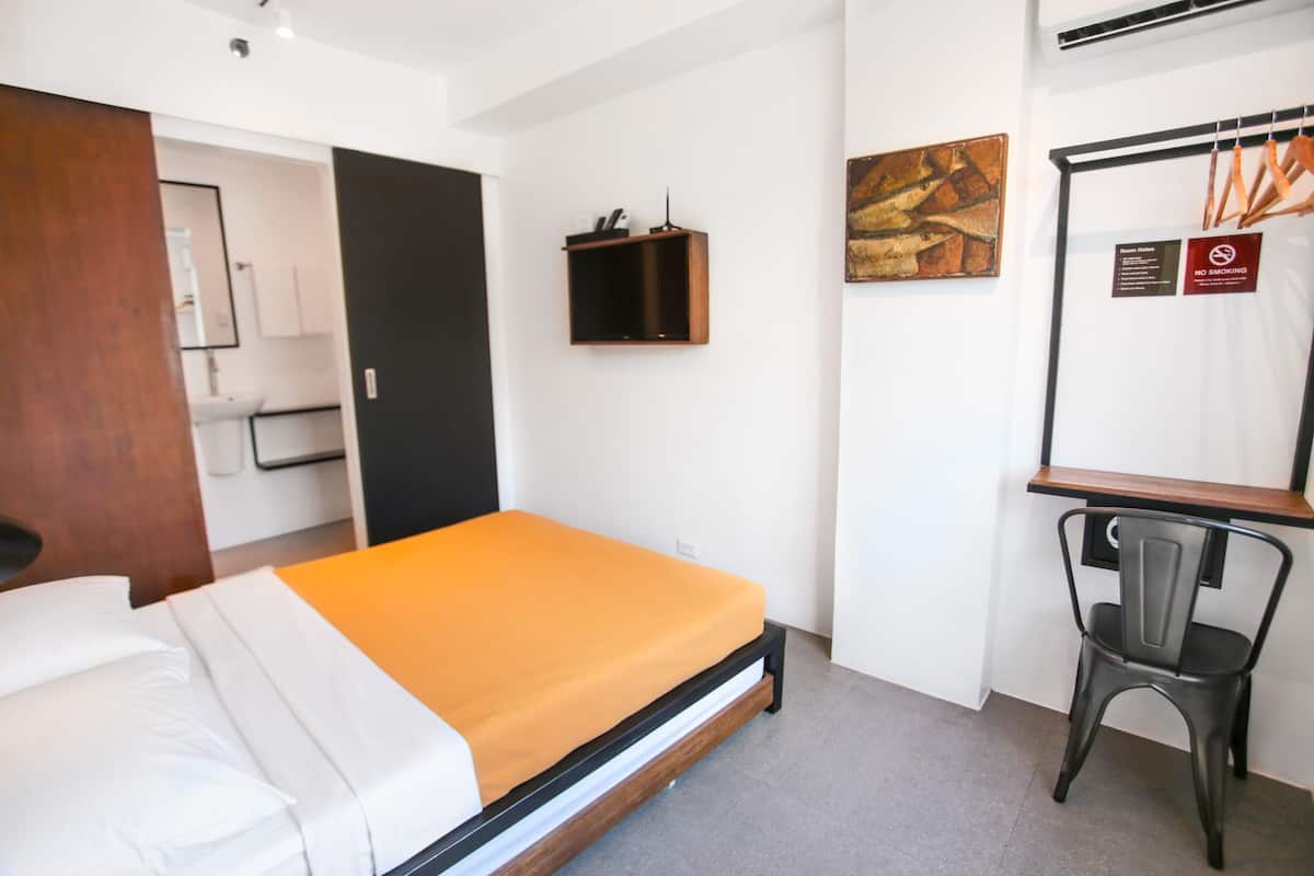 A hotel room with a bed, a desk, a chair, and a small shelf.