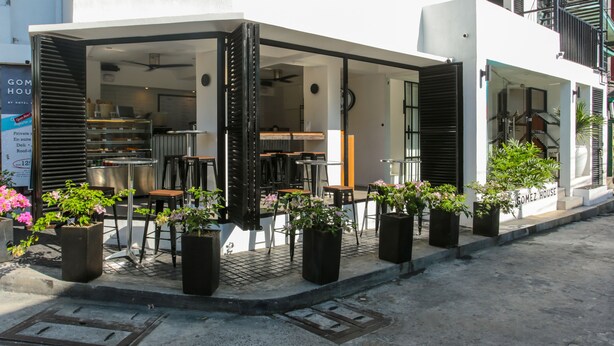 A modern hotel with an outdoor seating area, a visible kitchen, and potted plants. - Gomez House (Makati)