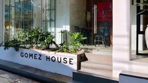 A modern building entrance with a glass facade, a white planter with greenery, and the name "Gomez House" displayed on the wall. - Gomez House (Makati)