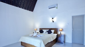 Un dormitorio con una cama de madera, dos mesitas de noche con lámparas, aire acondicionado instalado en la pared y una puerta.