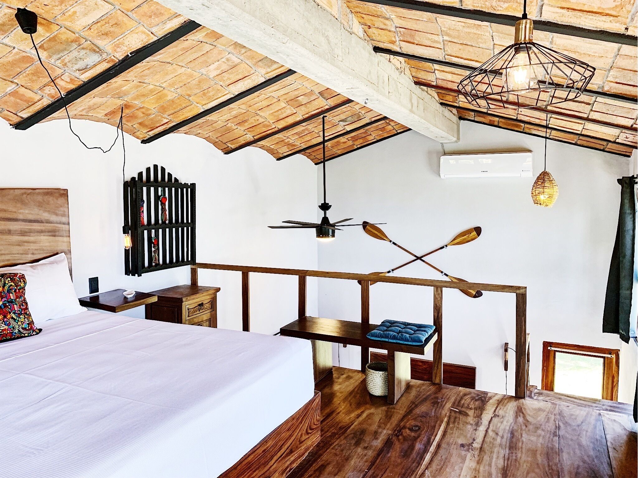 Un dormitorio con techo de madera, una cama, un escritorio con silla y una lámpara colgante.