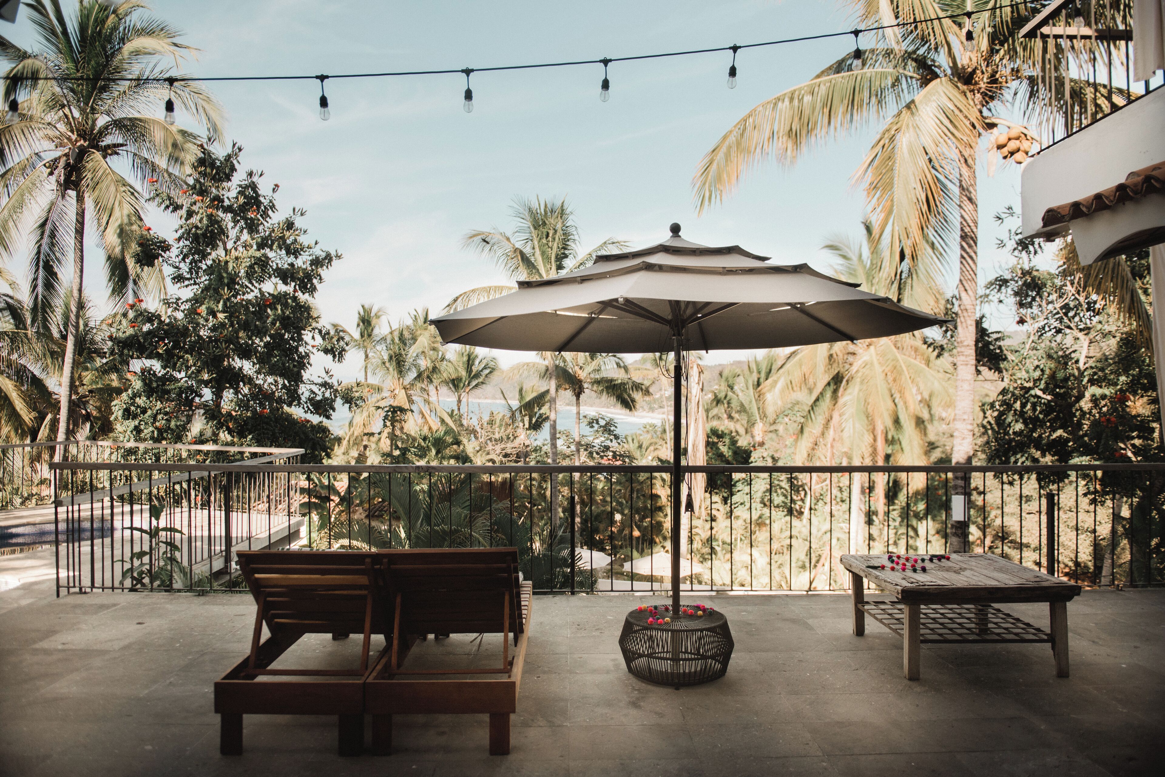 A balcony with a wooden bench, a round table with a woven basket, and a large umbrella.