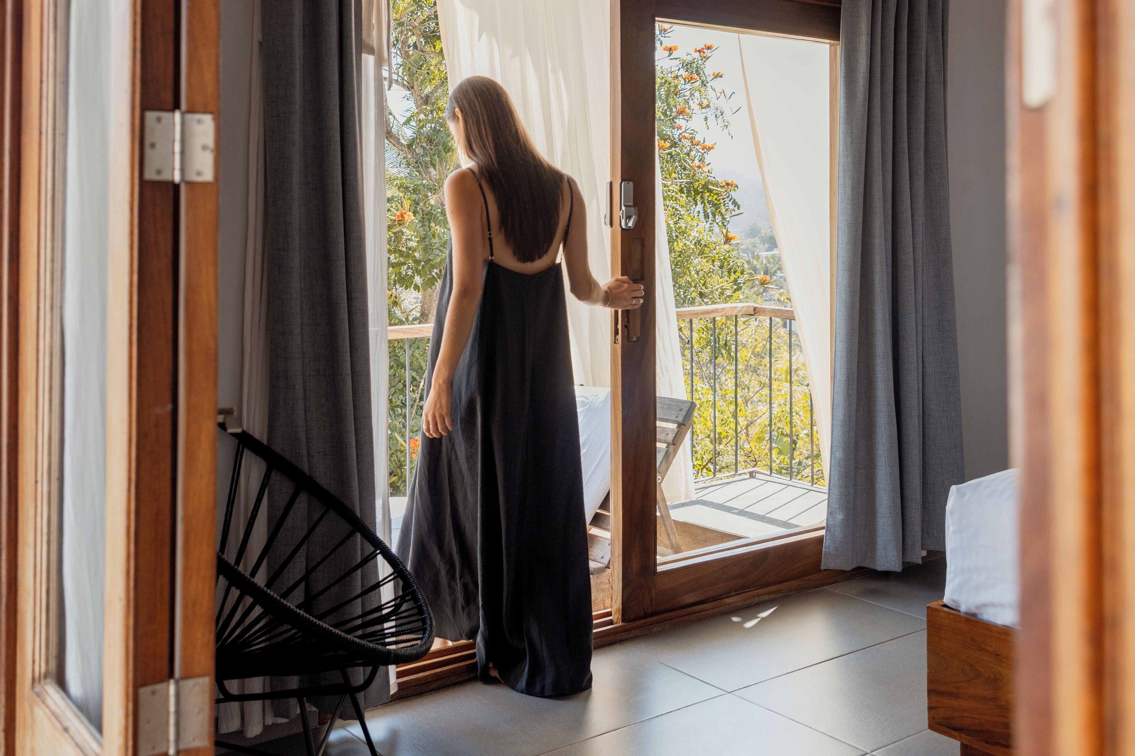 Una habitación con una puerta corrediza de vidrio que da a un balcón con vistas a árboles y una terraza de madera.