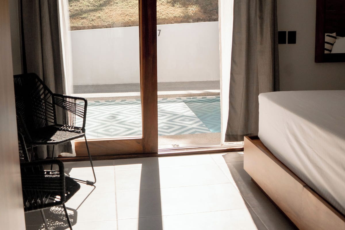 A room with a bed, a chair, a sliding glass door leading to a pool, and a view of the outdoors.