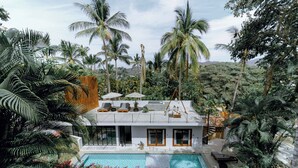 Una moderna casa con piscina, immersa in vegetazione tropicale e palme.