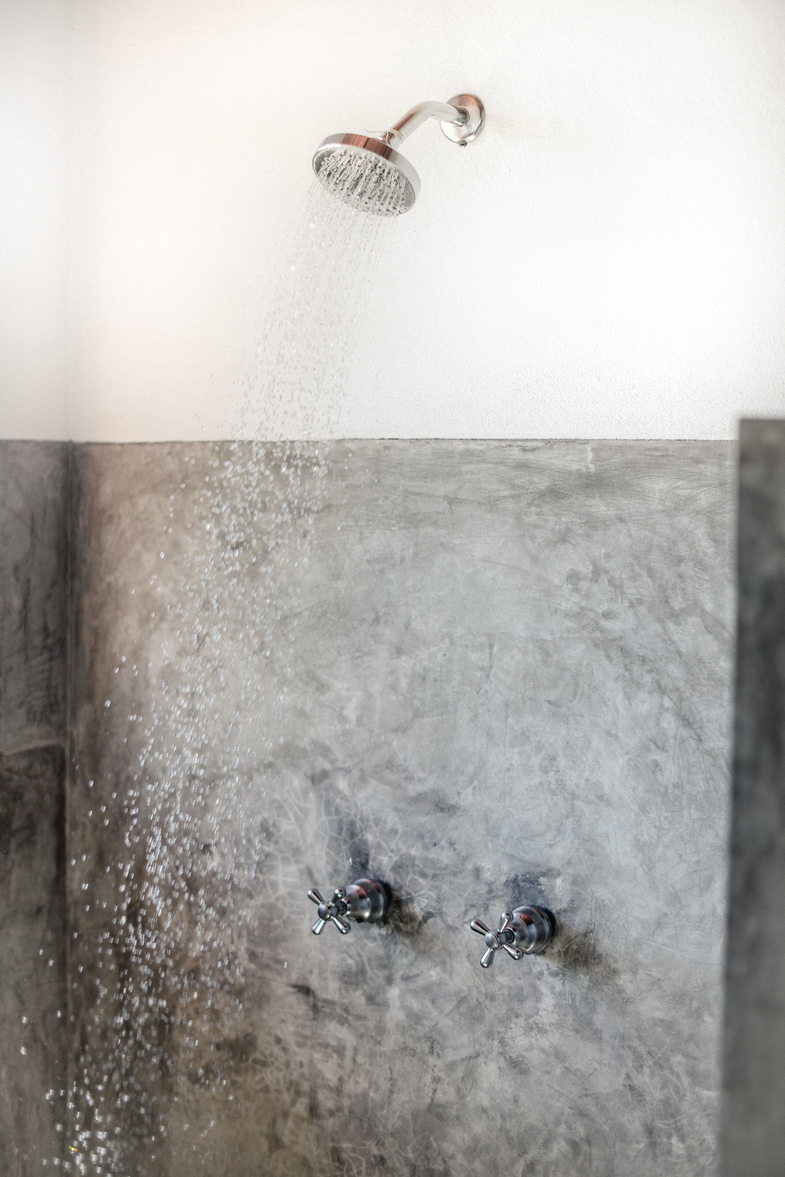 A shower with water flowing from a head-mounted showerhead, installed in a concrete wall.