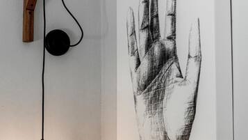 Una lámpara de pared con base de madera y cable negro, junto a una obra de arte con una huella de mano blanco y negro firmada por el artista.