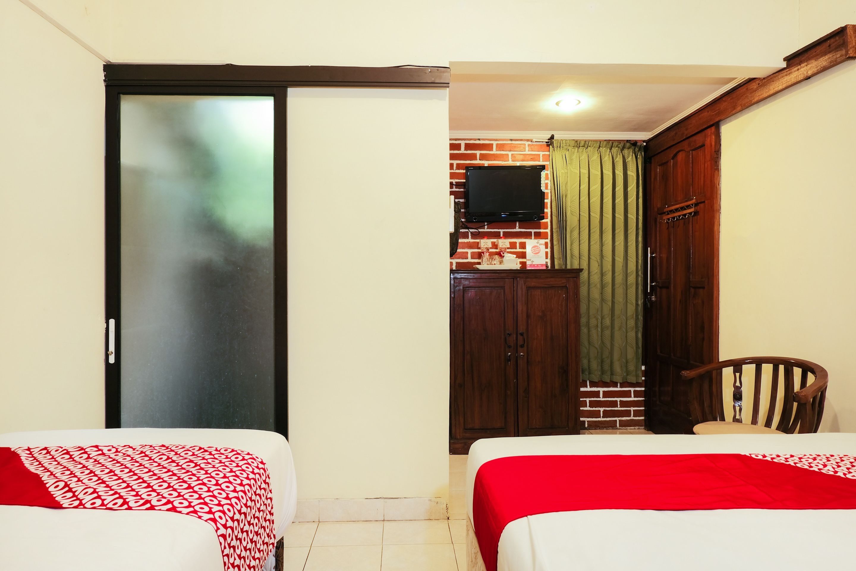 Une chambre d’hôtel avec deux lits, une télévision, une armoire et un mur en briques.