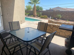 Eine Terrasse im Freien mit Tisch und Stühlen, einer Steinmauer, einem Pool und einem Grill.