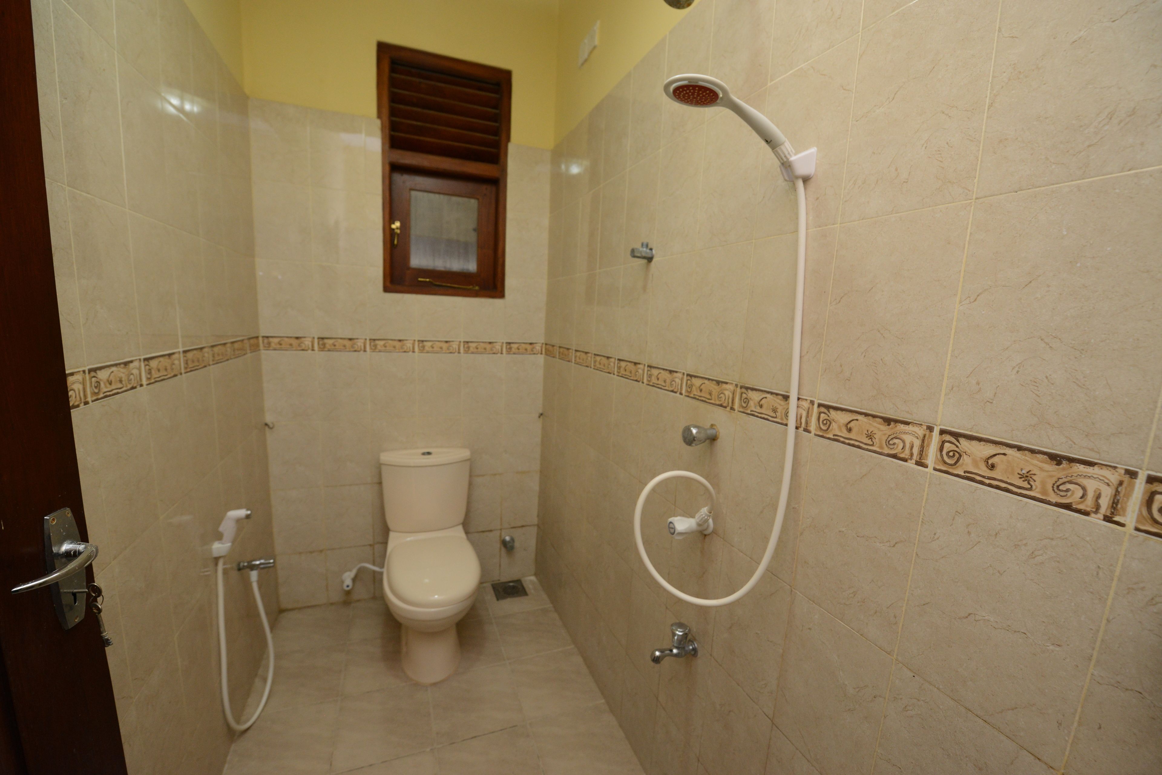 A bathroom with a toilet, shower, and a window.