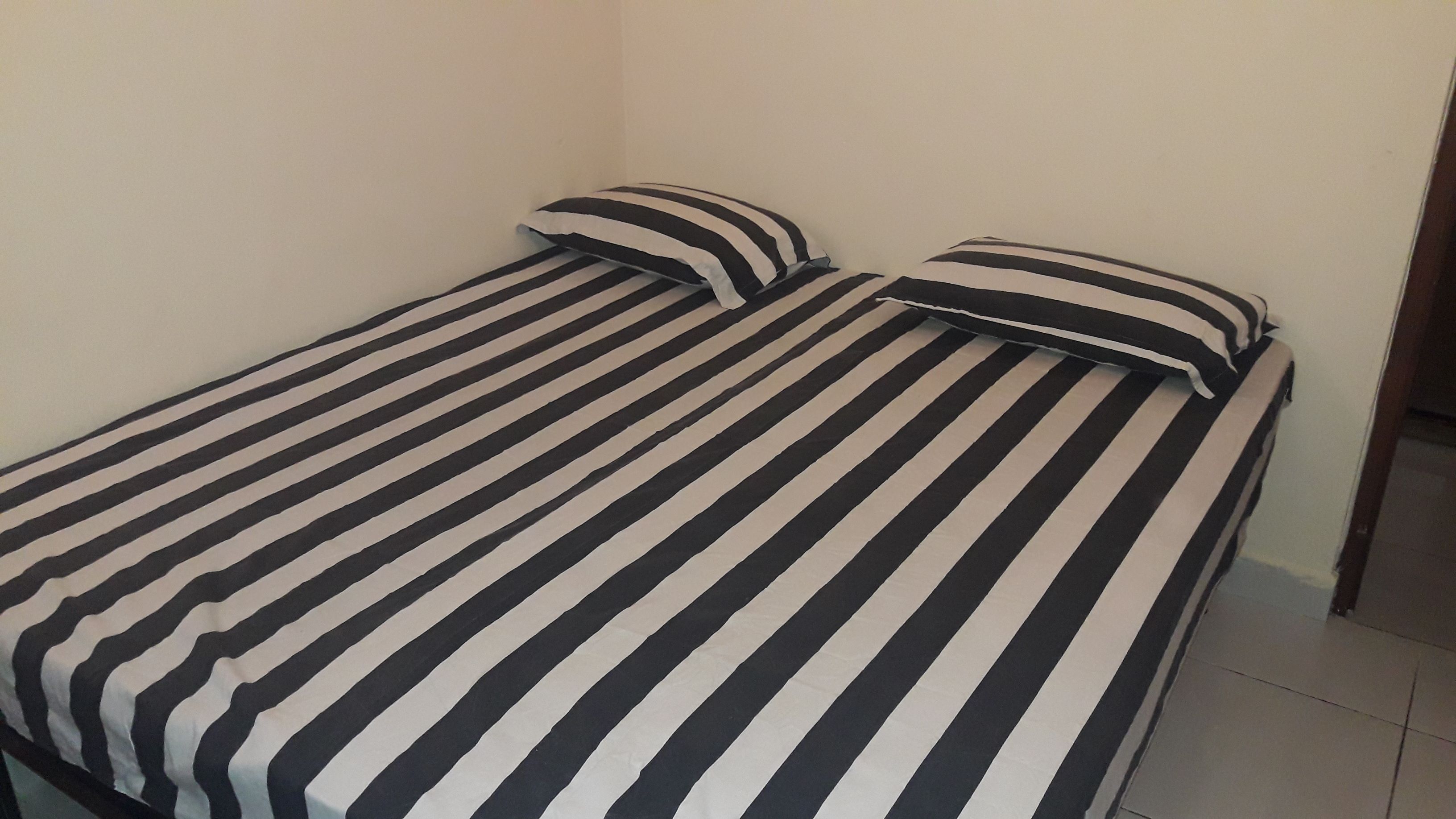 Een eenpersoonsbed met zwart-wit strepen dekbed in een kamer met witte wanden.