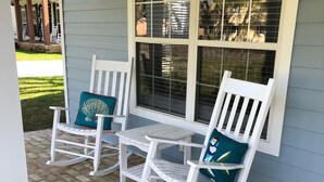 A porch with two rocking chairs and a small table, a brick floor, and a window with blinds. - BSL Living - Across from Pickleball Courts, Splash Pad and Park - Permit #BSL140 (Bay St Louis)