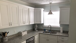 A kitchen with white cabinets, a granite countertop, a coffee maker, and a dishwasher. - BSL Living - Across from Pickleball Courts, Splash Pad and Park - Permit #BSL140 (Bay St Louis)