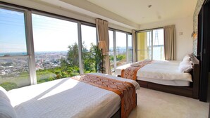 Habitación de hotel con dos camas, ventanas amplias y vista a un paisaje urbano.