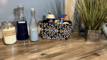 Une surface en bois sur laquelle se trouvent un bocal en verre étiqueté « Savon à lessive », une bouteille étiquetée « Détergent à lessive », une bouteille étiquetée « Adoucissant » et un sac à motifs noir et blanc contenant un flacon pulvérisateur et un récipient.