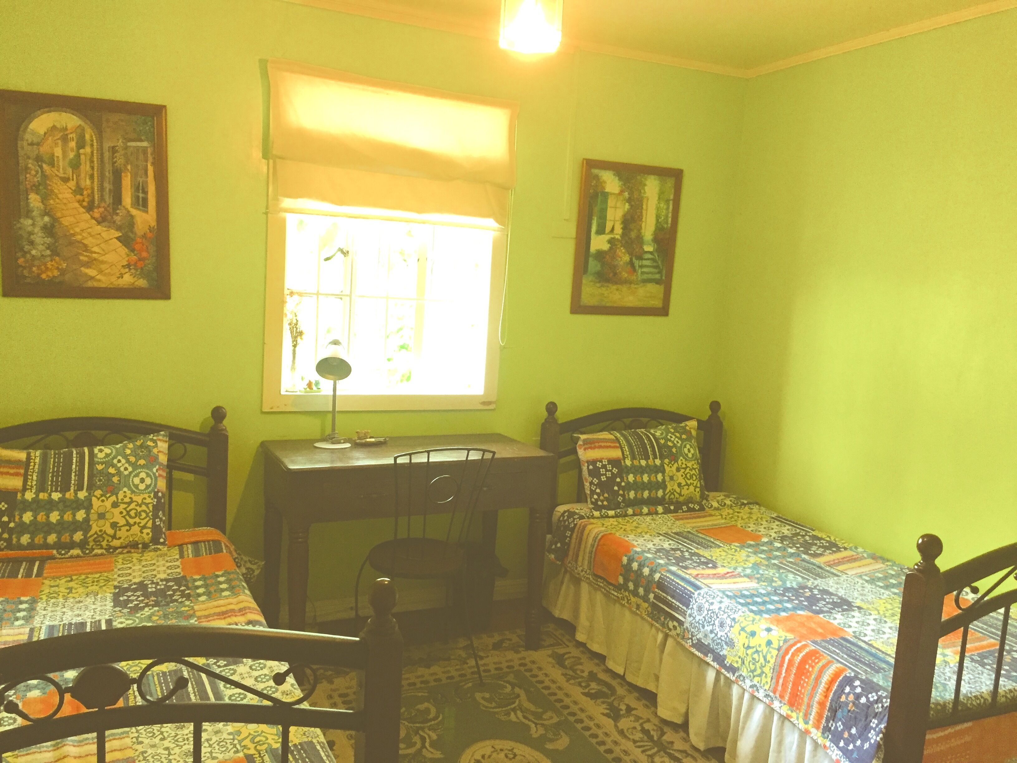 A room with two single beds, a desk, and a window with a view of a street.
