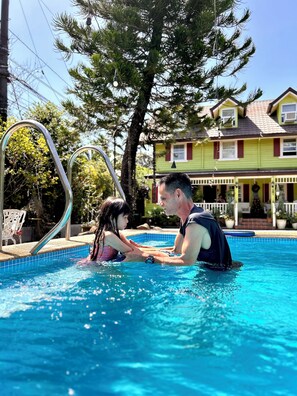 Una piscina amb una escala metàl·lica, envoltada d'arbres i una casa al fons.