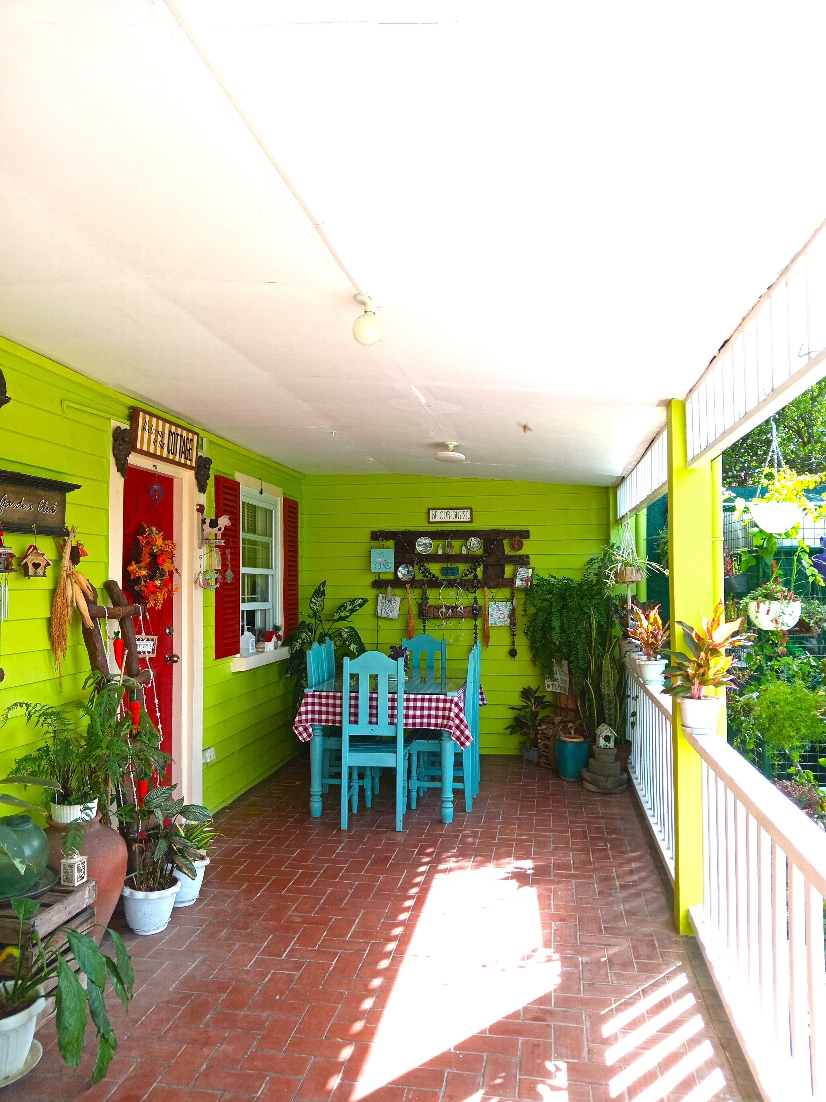 A bright green porch with a red door, a table with a checkered tablecloth, and several potted plants.