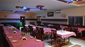 A restaurant with multiple tables, each covered with a pink tablecloth and set with plates and cutlery. The ceiling features recessed lighting and wooden beams.