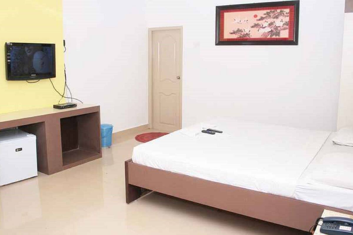A bedroom with a bed, a TV mounted on a wall, a small desk with a computer, and a door.