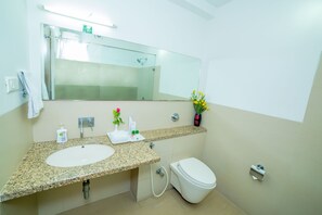 A bathroom with a granite countertop sink, a mirror, a toilet, and a vase with flowers. - Park Inn Beach Resort (Chennai)