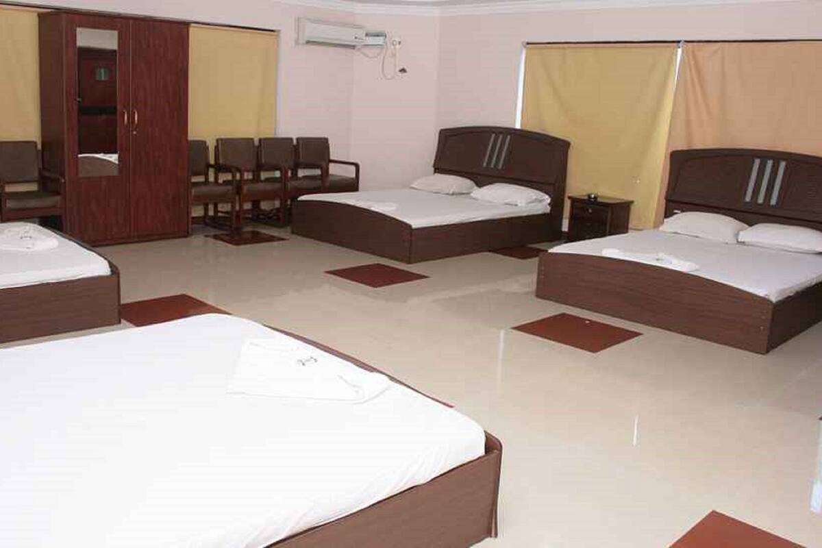 A hotel room with three beds, a wardrobe, a desk, and a chair.