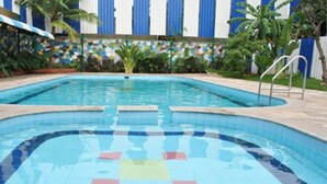 A swimming pool with clear blue water, surrounded by a tiled deck and palm trees.