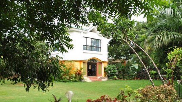 A white house with a red door, surrounded by lush greenery and a well-maintained lawn.