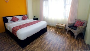 Una habitación de hotel con una cama grande, una silla, una mesita y una ventana con cortinas.