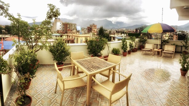 Una terraza en la azotea con suelo de baldosas, mobiliario de mimbre y plantas en macetas.