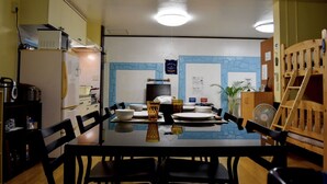 Een eetgedeelte met een tafel voor vier personen, stoelen, een koelkast, een magnetron en een houten bank.