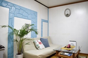 Una habitación con sofá, una mesita de centro de vidrio, una planta en maceta y un reloj de pared.