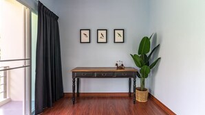 A room with a wooden floor, a dark-colored table with drawers, a large green plant, and three framed pictures on the wall.