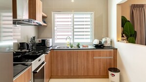 A compact kitchen with wooden cabinets, a built-in stove, a microwave, and a window with blinds.