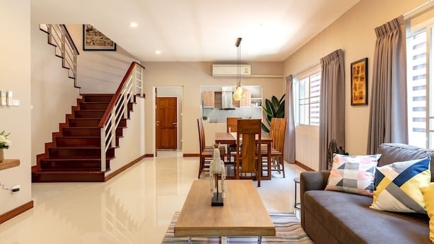 A modern living room with a wooden staircase, a dining area, and a kitchen in the background.
