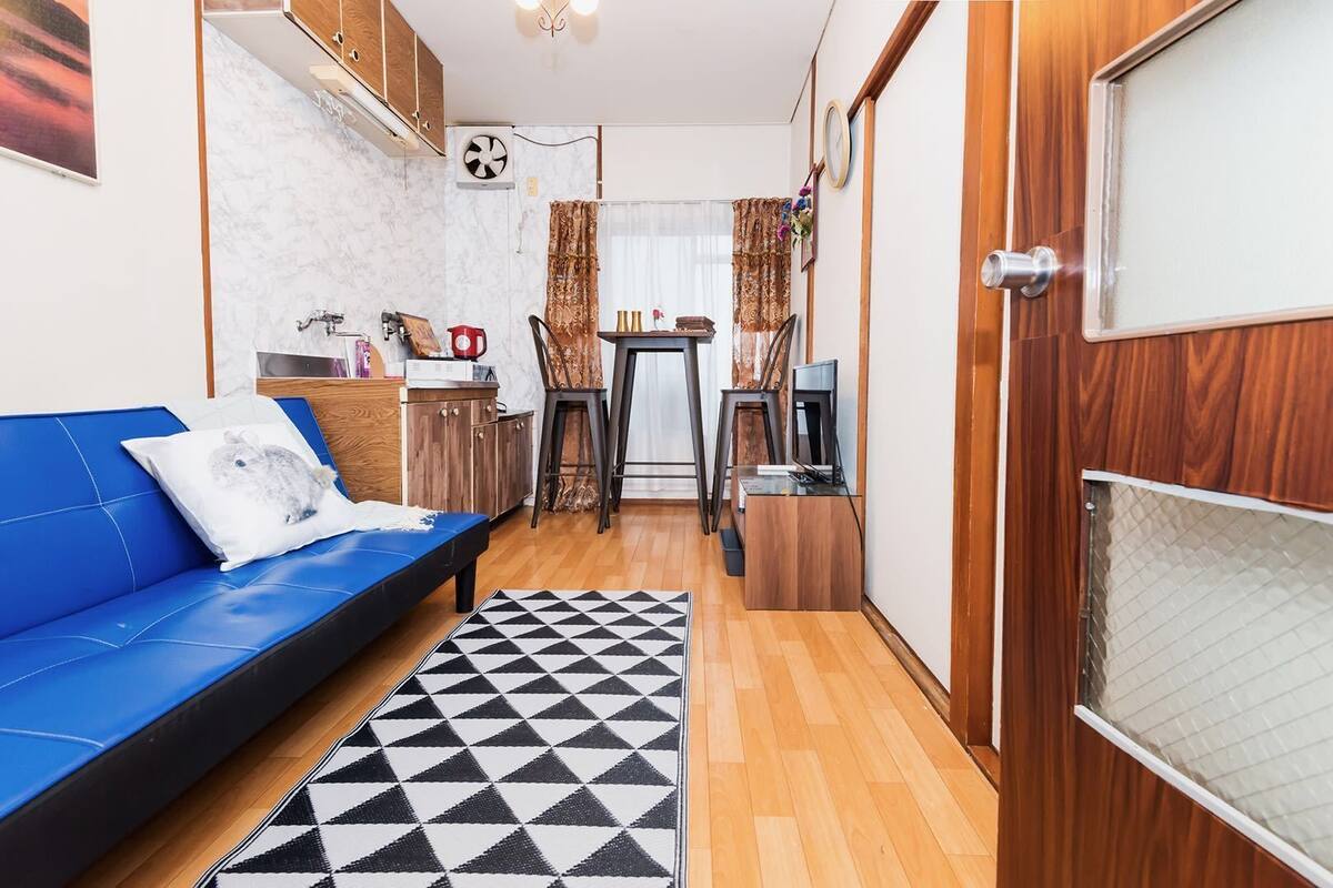 A compact living space with a blue sofa, a small dining table, and a kitchen area.