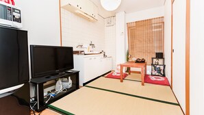 Un espace de vie compact comprenant un téléviseur posé sur un meuble, une kitchenette équipée d’un four à micro-ondes et un coin repas avec une table et des chaises.
